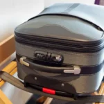 A gray suitcase in a hotel room sitting on a suitcase rack.