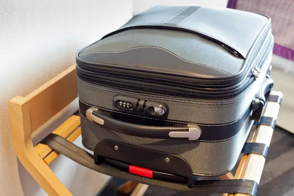 A gray suitcase in a hotel room sitting on a suitcase rack.