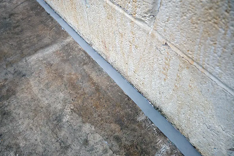 Flexi Armour caulking being used by Suburban Exterminating to seal the gap crack space between a concrete floor & brick wall.