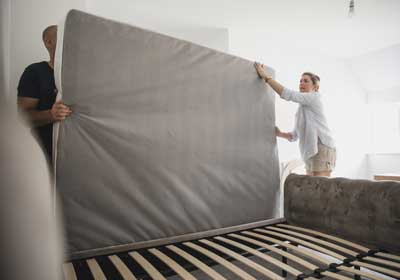 Two people lifting mattress off of frame