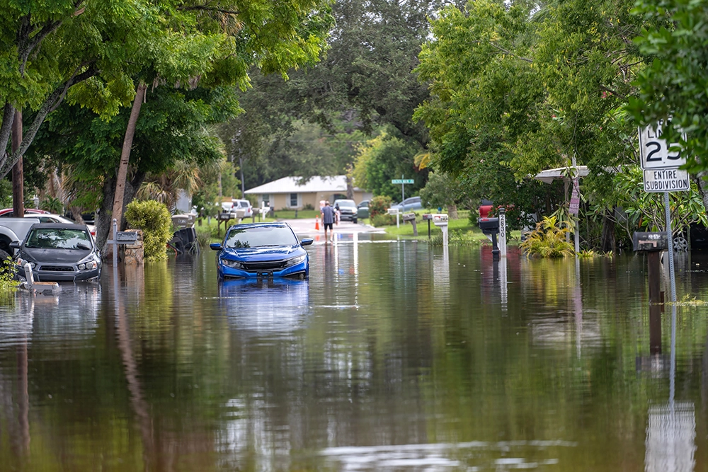 A residential neighborhood struggling with several inches of floodwater, submerging cars.
