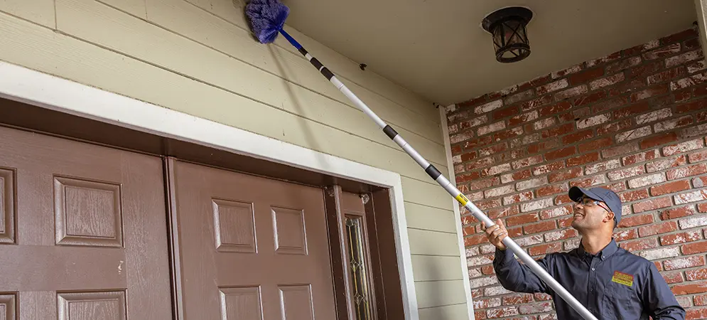 Tech cleaning above the front door of a house | Suburban Exterminating Pest Control serving Ronkonkoma, NY